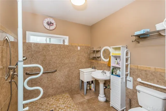 An accessible bathroom with a roll-in tiled shower, grab bars, and a pedestal sink